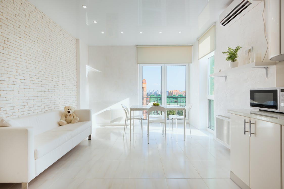 A Living Room and Kitchenette with an All-White Color Scheme and a Wall-mounted Air Conditioning Unit