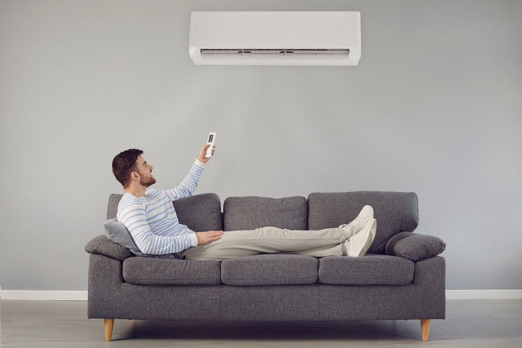 Man on the couch turning on AC while assessing common AC issues.