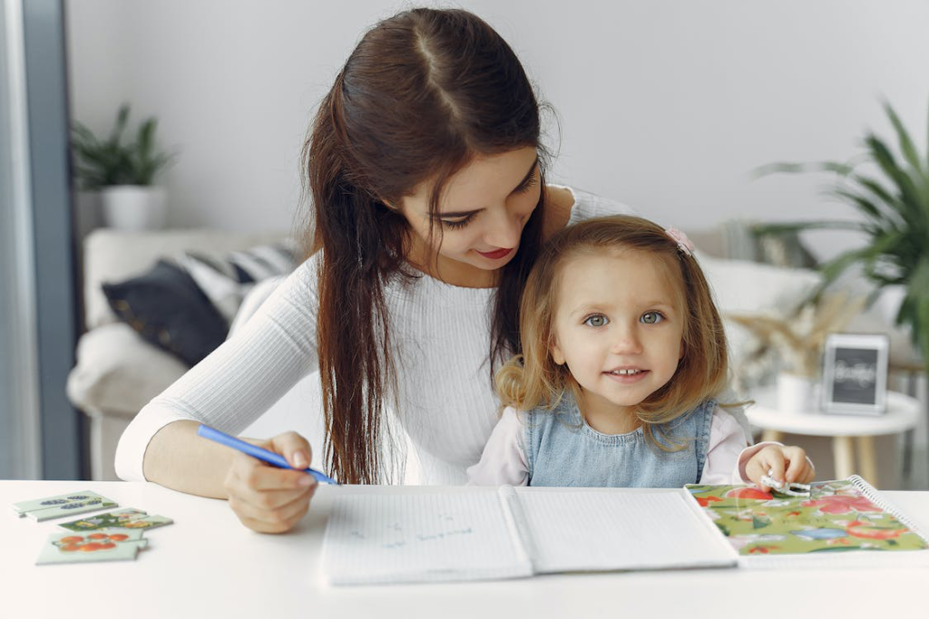 Woman in White Long Sleeve Shirt Holding Girl in White Shirt Writing on White Paper